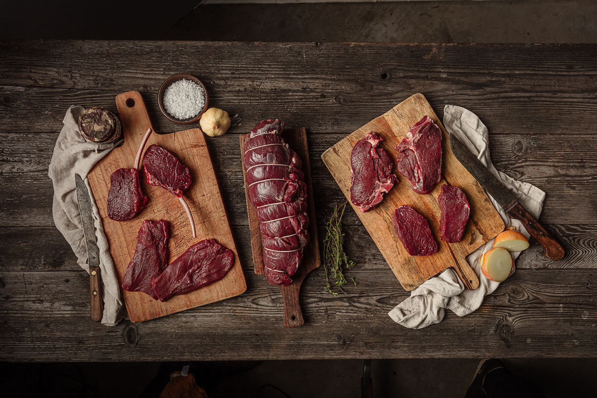 Wild venison steaks and a rolled venison joint on rustic wooden boards